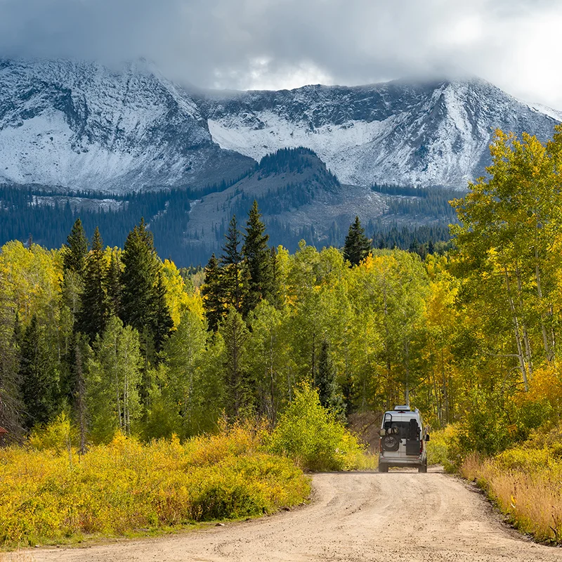 crested_butte_1730510379 Camper van on dirt road with beautiful fall foliage scenery of snowcapped Rocky mountain, yellow aspen and pine trees in Gunnison National Forest near Crested Butte, Colorado