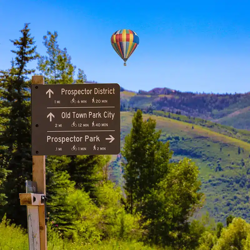 park_city_365337281 a hot air balloon flies above a sign with directions to places in Park City, Utah